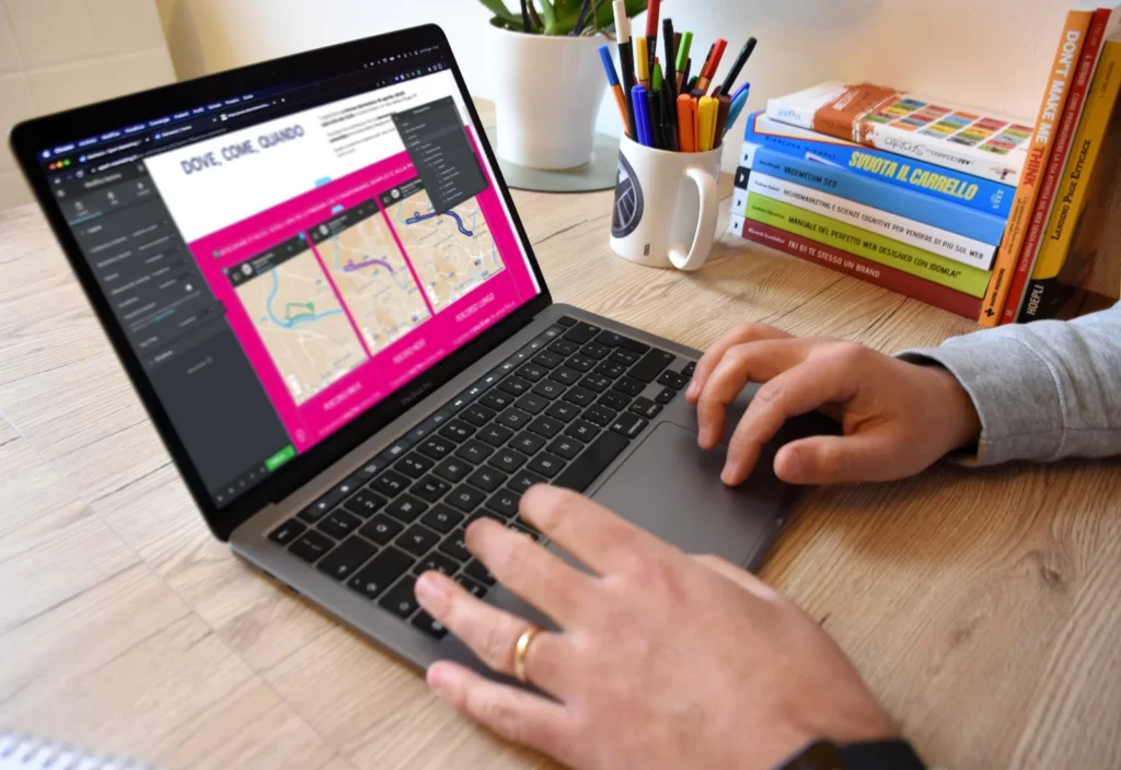 Fasi di lavoro al computer su una scrivania in legno sulla quale sono posati libri di marketing, una tazza porta biro e una pianta verde